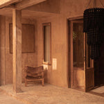 A rustic interior with a wooden chair and open door leading to a garden with extra large black chandelier