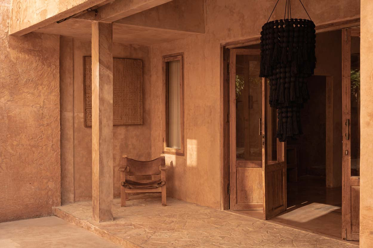 A rustic interior with a wooden chair and open door leading to a garden with extra large black chandelier