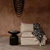 Black wooden bead chandelier hanging from ceiling in a terracotta plastered room with linen chair and throw