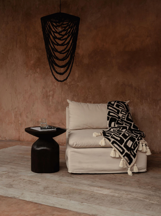 Black wooden bead chandelier hanging from ceiling in a terracotta plastered room with linen chair and throw