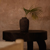 Dark wooden table with a textured vase and a single leaf on a beige background