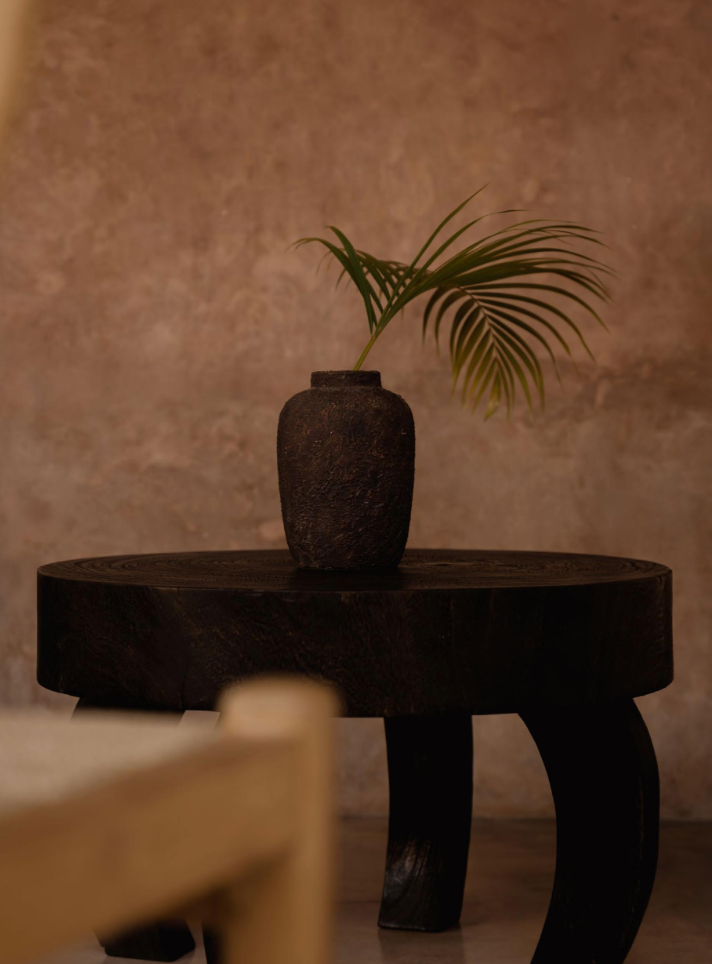 Dark wooden table with a textured vase and a single leaf on a beige background