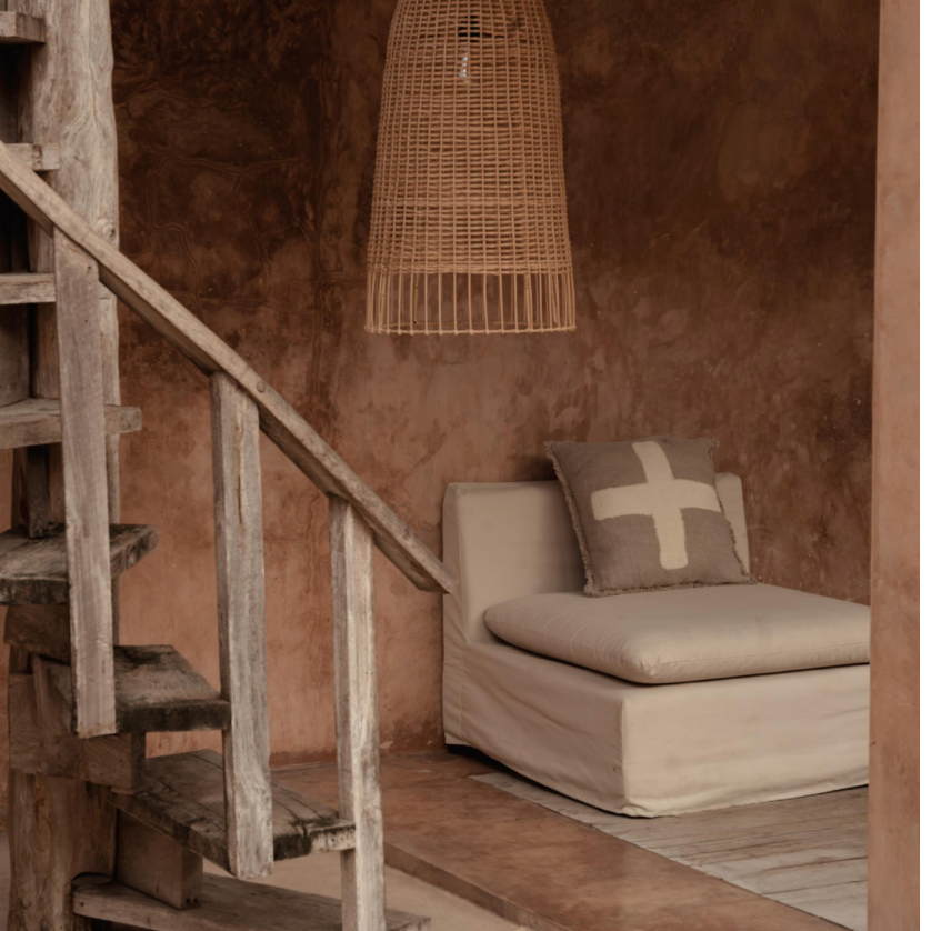 Design interior with a textured plastered wall, wooden staircase, and a cushioned chair and extra large rattan pendant light