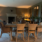 Dining room with wooden table and rattan wicker dining chairs, fireplace, and plants.
