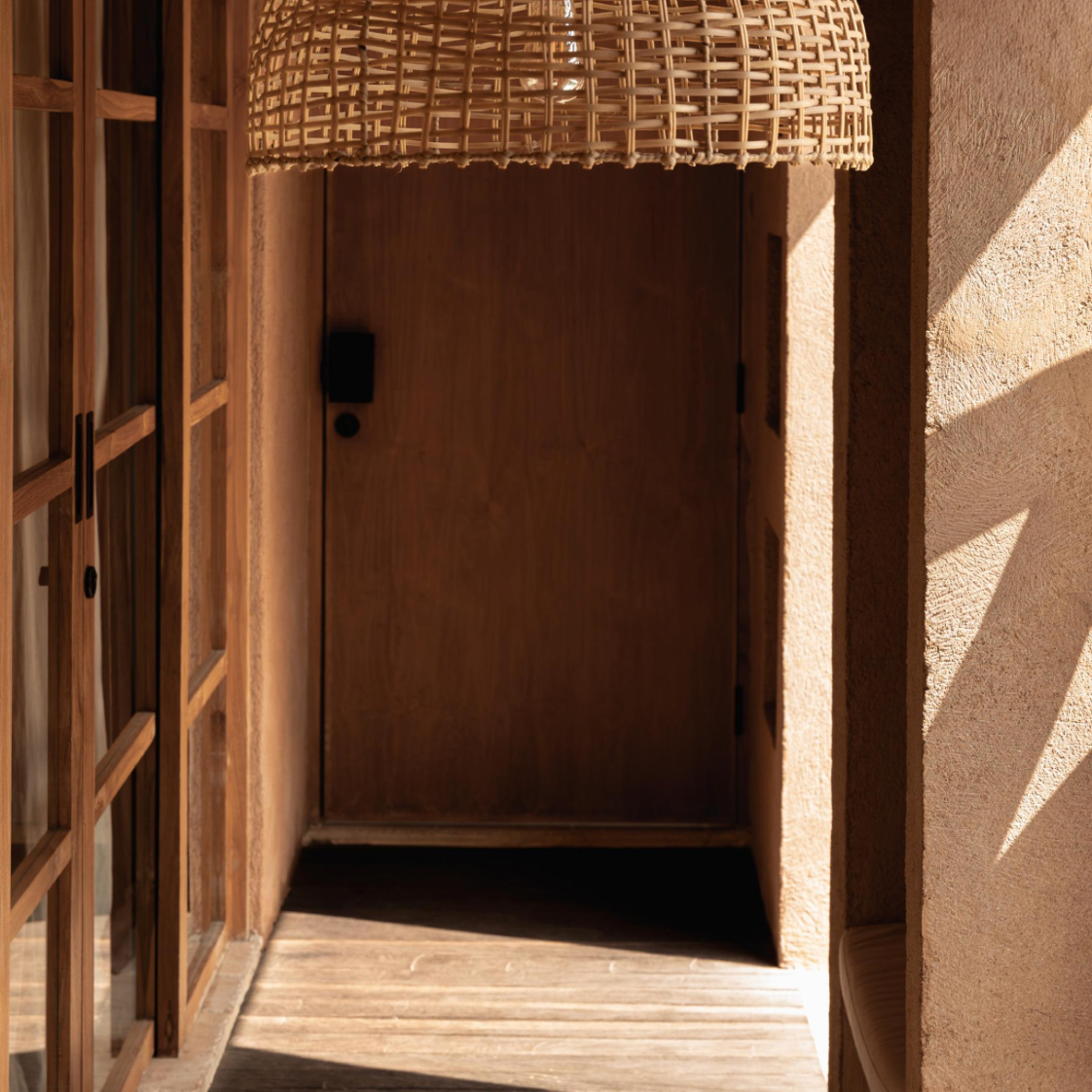Woven synthetic rattan pendant light hanging in a room with wooden shelves and textured walls.
