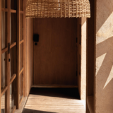 Woven synthetic rattan pendant light hanging in a room with wooden shelves and textured walls.