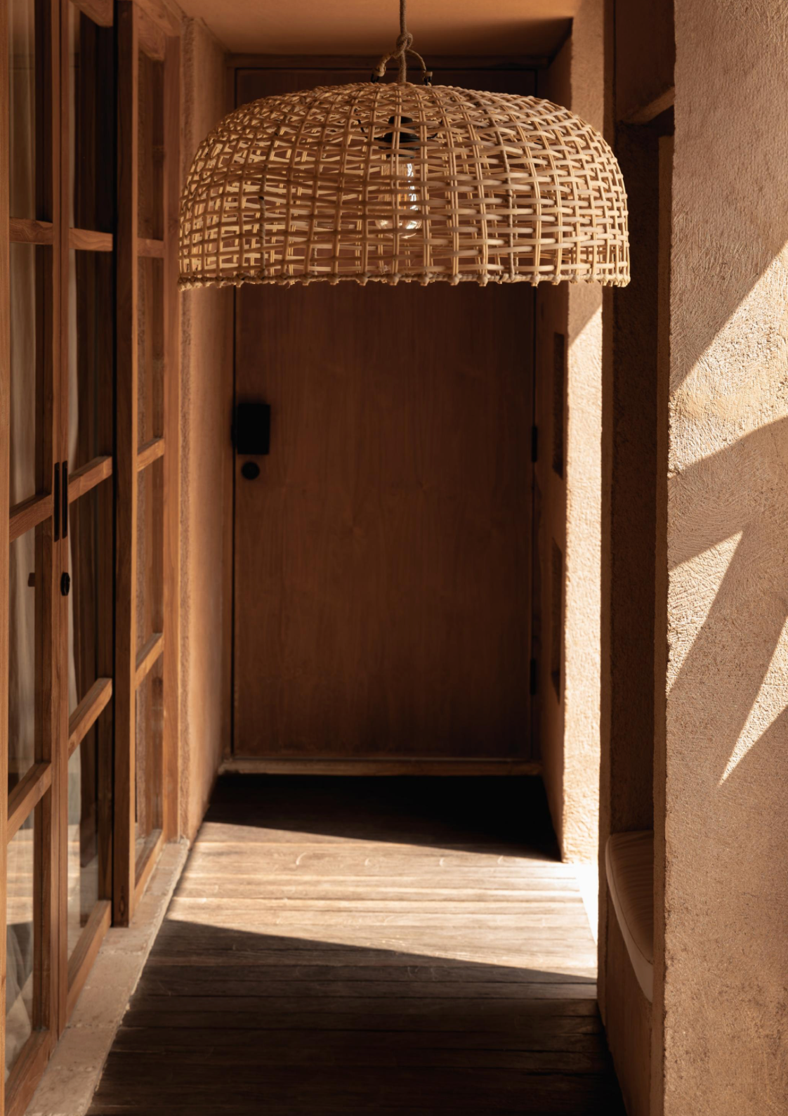 Woven synthetic rattan pendant light hanging in a room with wooden shelves and textured walls.