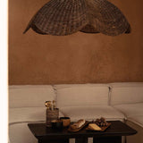 Extra Large Rattan Wicker pendant light shade hanging above a coffee table with decor items in a room with a beige sofa and wall.