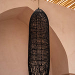 large Black woven rattan  pendant light hanging against a beige wall with a textured ceiling.