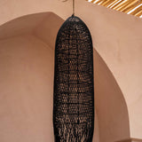 large Black woven rattan  pendant light hanging against a beige wall with a textured ceiling.