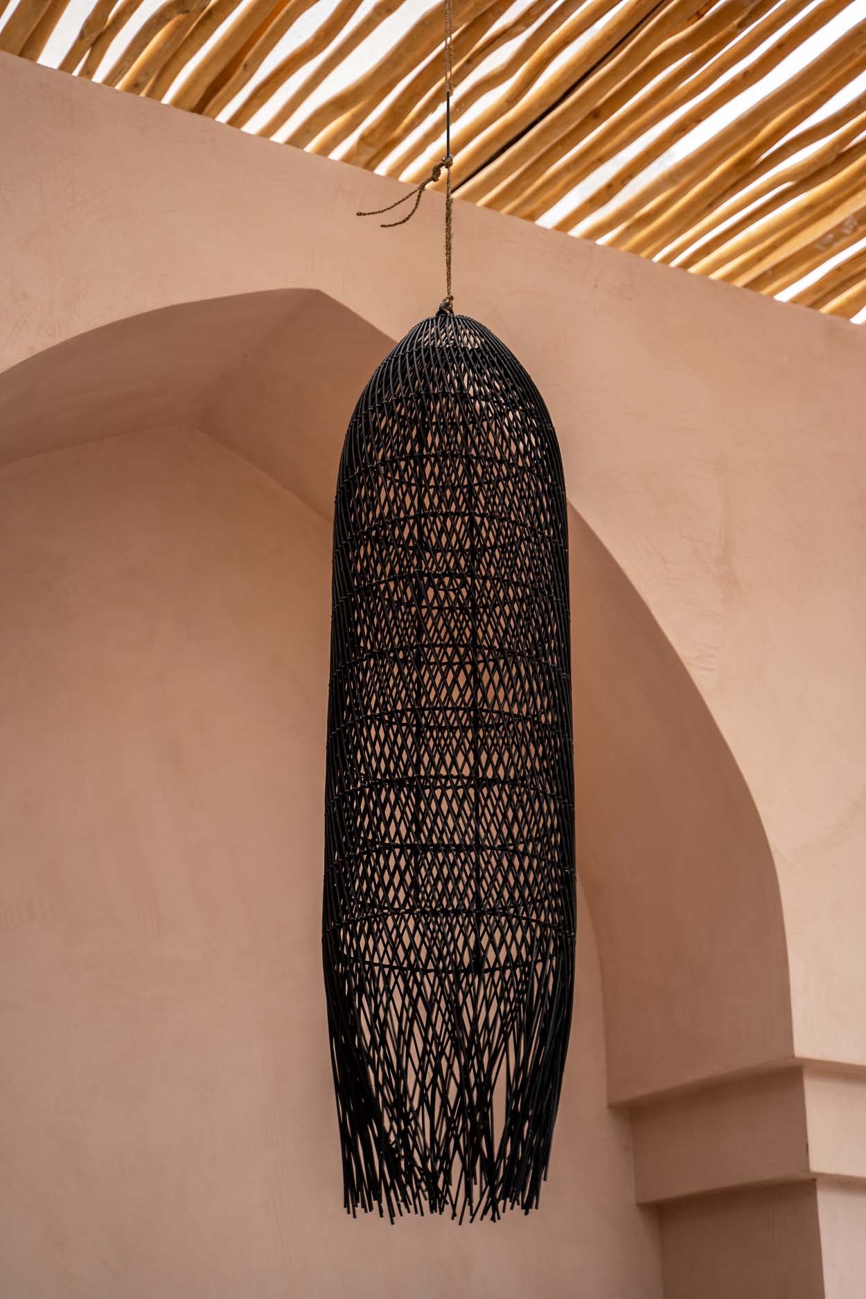 large Black woven rattan  pendant light hanging against a beige wall with a textured ceiling.