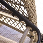 Close-up of a wicker outdoor lounger chair with black metal frame on a textured surface.