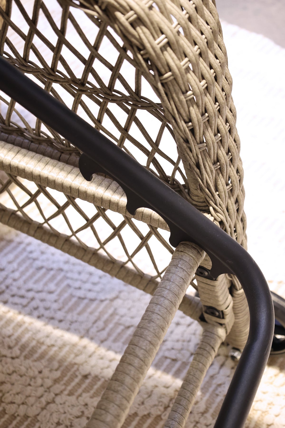 Close up of a wicker outdoor lounger chair with black metal frame on a textured surface.