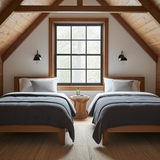 Two beds  with cotton  navy blue throws in a room with wooden beams and a large window.