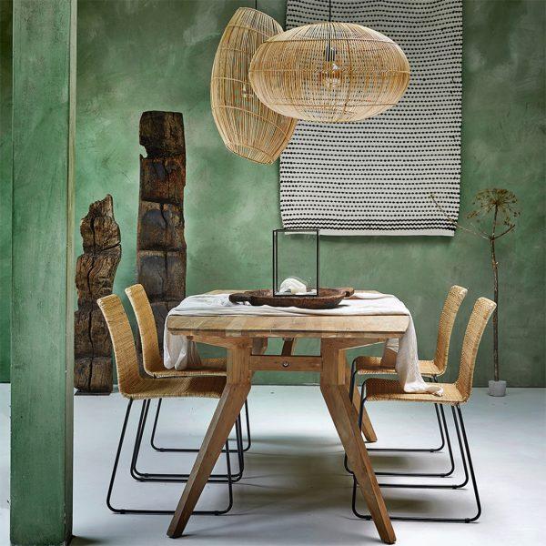 Rattan lights hanging over dining table with wooden table and chairs against a green wall.
