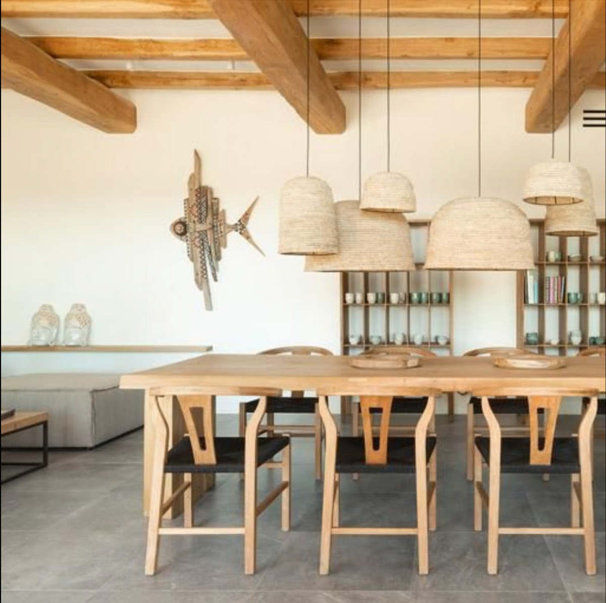 A large natural raffia rattan large light shade hanging above a dining table   uk