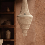 Handmade Shell chandelier  hanging against a textured wall with wooden shelves in the background.