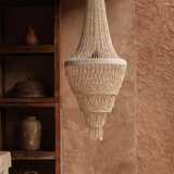 Handmade Shell chandelier  hanging against a textured wall with wooden shelves in the background.