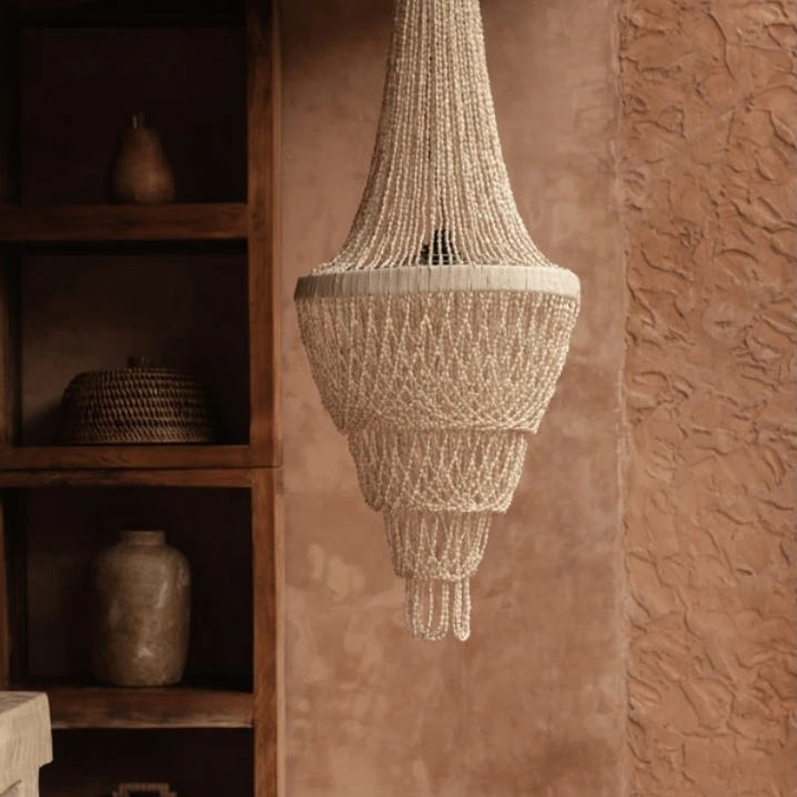 Handmade Shell chandelier  hanging against a textured wall with wooden shelves in the background.