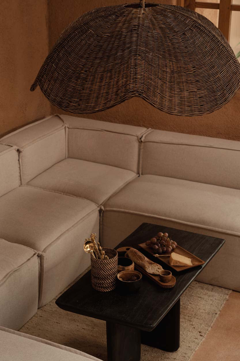 Beige sectional sofa with a dark coffee table and wicker rattan large pendant light shade in a warm-toned room.