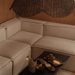 Beige sectional sofa with a dark coffee table and wicker rattan large pendant light shade in a warm-toned room.