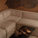 Beige sectional sofa with a dark coffee table and wicker rattan large pendant light shade in a warm-toned room.
