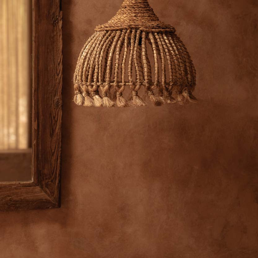Woven natural grass pendant light hanging against a textured brown wall. UK