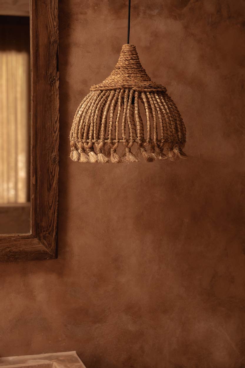 Woven natural grass pendant light hanging against a textured brown wall. uk