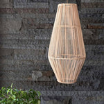 A natural woven rattan pendant light hangs against a dark gray stone wall, with green foliage visible in the lower left corner.