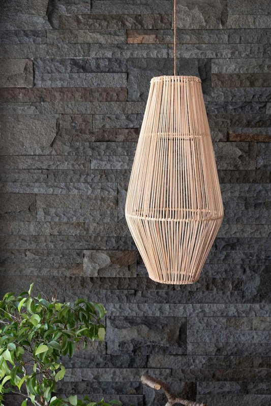 A natural woven rattan pendant light hangs against a dark gray stone wall, with green foliage visible in the lower left corner.