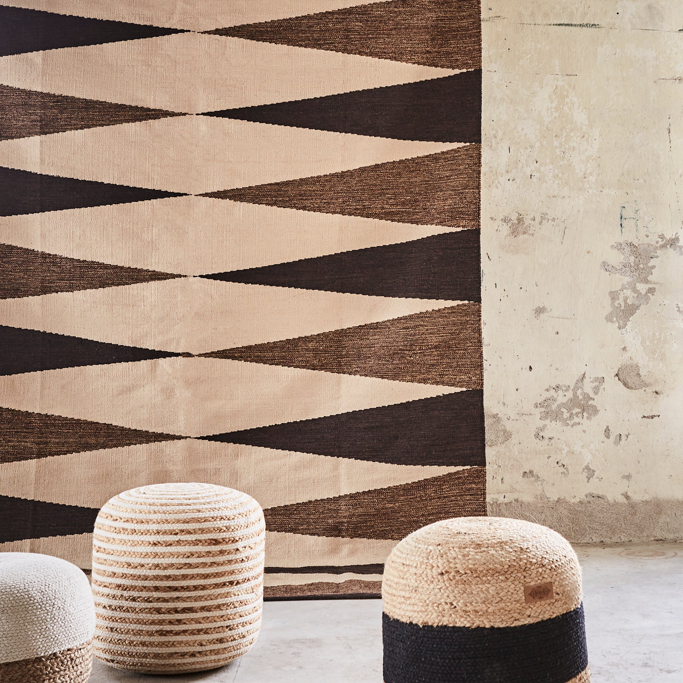 Geometric patterned rug with striped stools against a textured wall.
