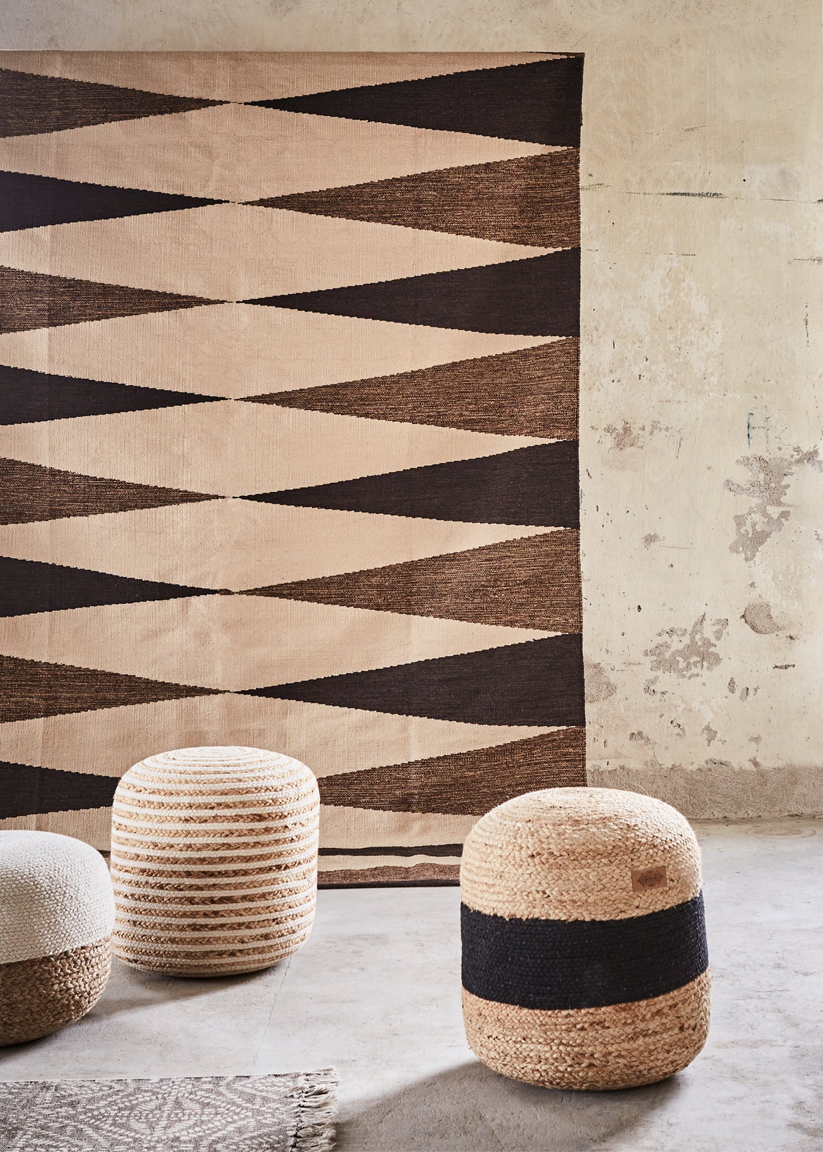 Geometric patterned rug with striped stools against a textured wall.