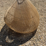 Textured brown rattan wicker basket shade on a gravel surface