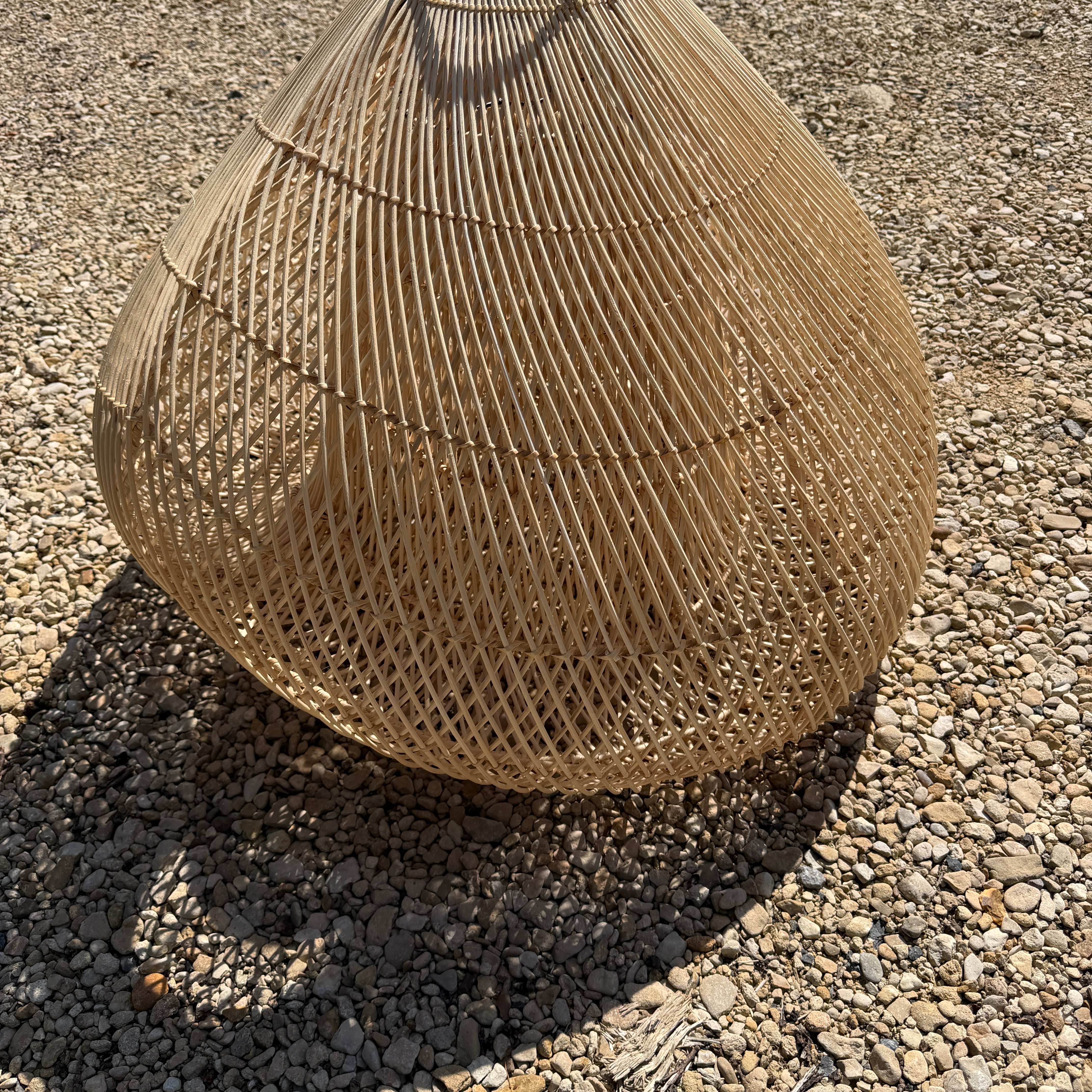 Textured brown rattan wicker basket shade on a gravel surface
