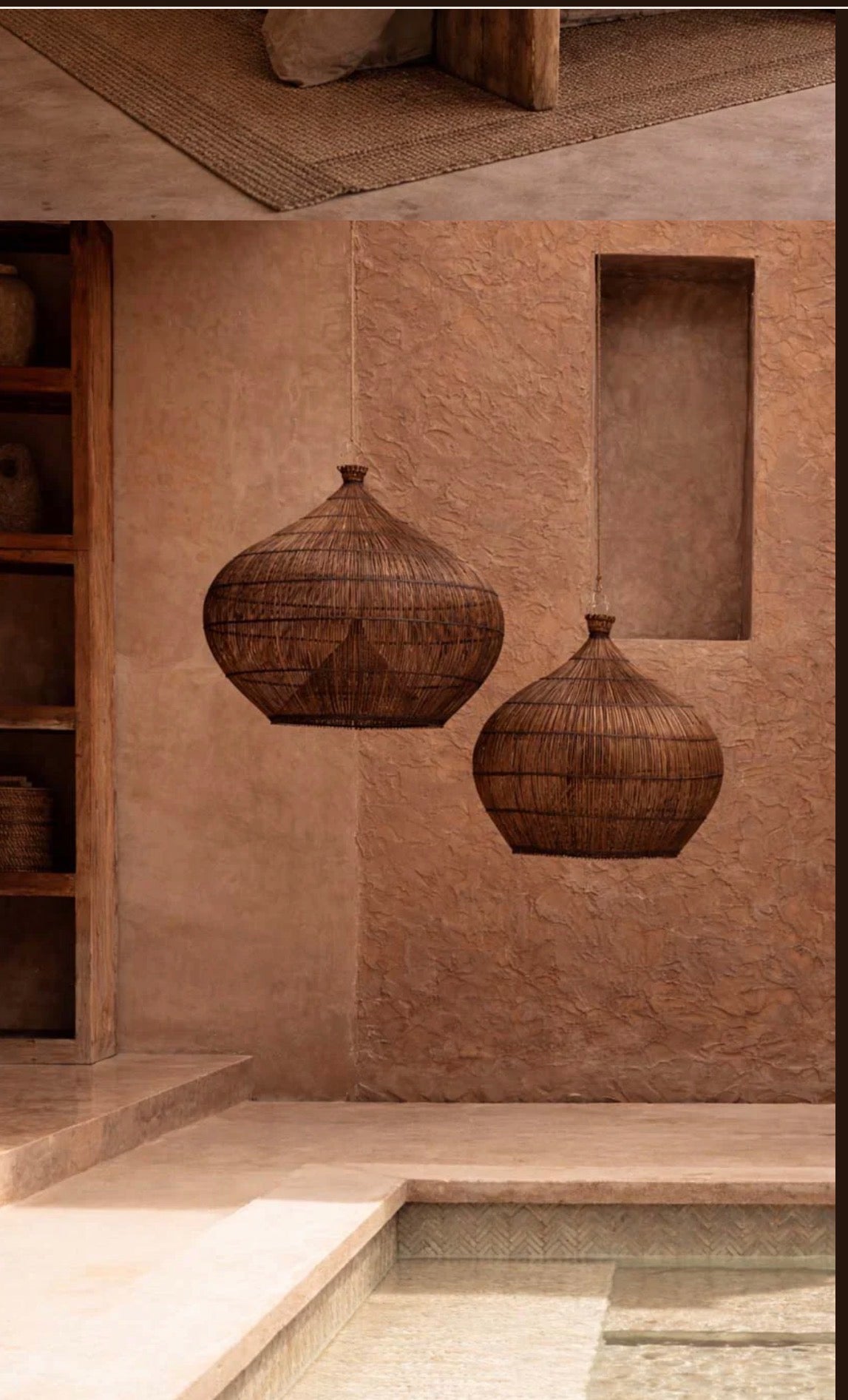 Two woven dark ration wicker penda nt lights hanging on a textured wall with a shelf and rug in the background.