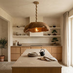 A rustic pendant light with a textured, organic-shaped brown shade and a twisted rope-style cord hangs over a modern kitchen island. The kitchen features light wood cabinets, open shelves with decorative items, and a stone countertop.