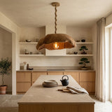 A rustic pendant light with a textured, organic-shaped brown shade and a twisted rope-style cord hangs over a modern kitchen island. The kitchen features light wood cabinets, open shelves with decorative items, and a stone countertop.