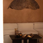 Extra large Wicker pendant light shade hanging above a coffee table with snacks on a beige sofa against a brown wall.