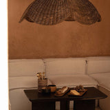 Extra large Wicker pendant light shade hanging above a coffee table with snacks on a beige sofa against a brown wall.
