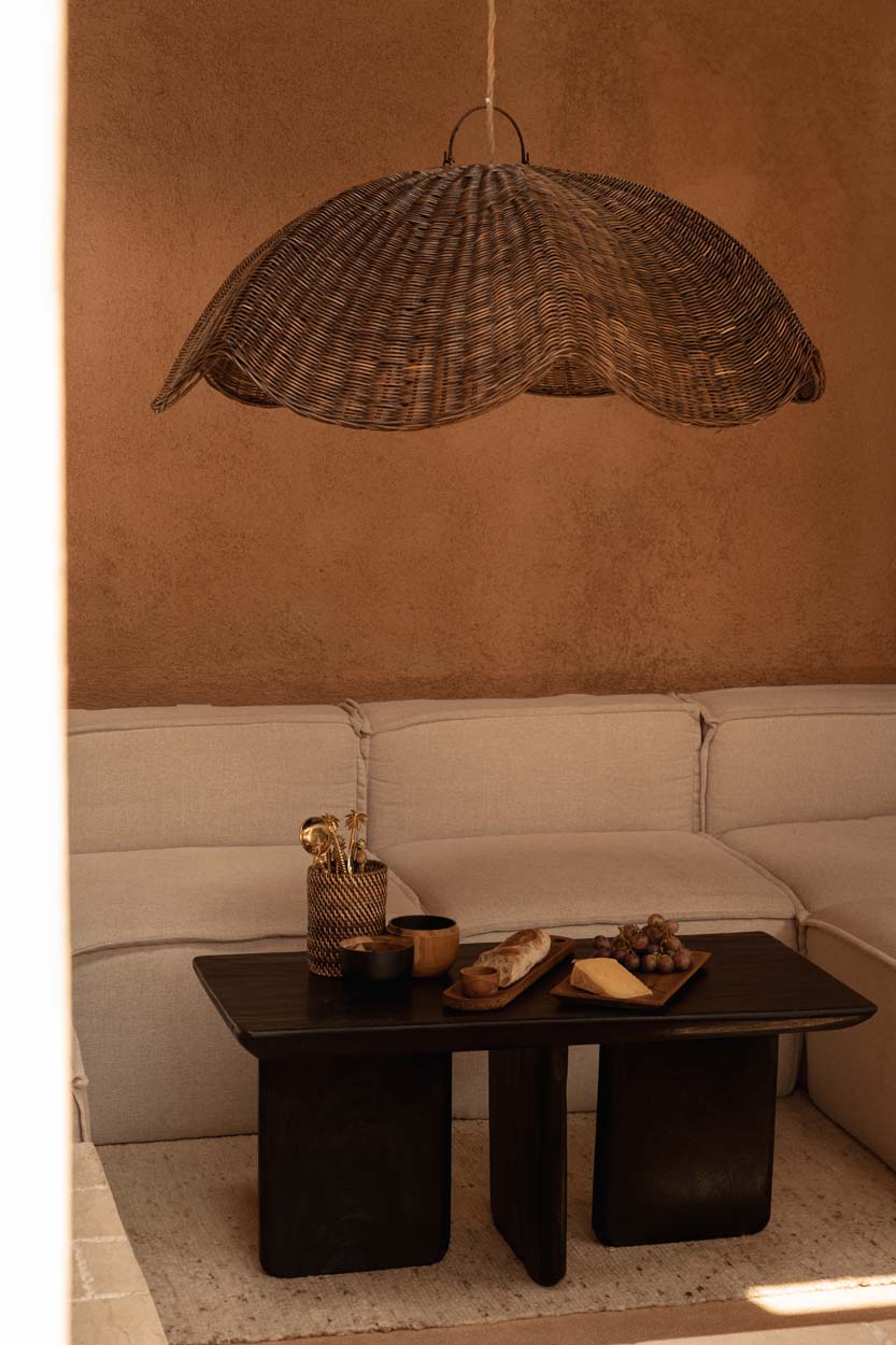 Extra large wicker pendant light shade hanging above a coffee table with snacks on a beige sofa against a brown wall.