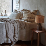 Cozs bedroom with textured bedding and stripe 50cm cushions, wooden nightstand with lamp 