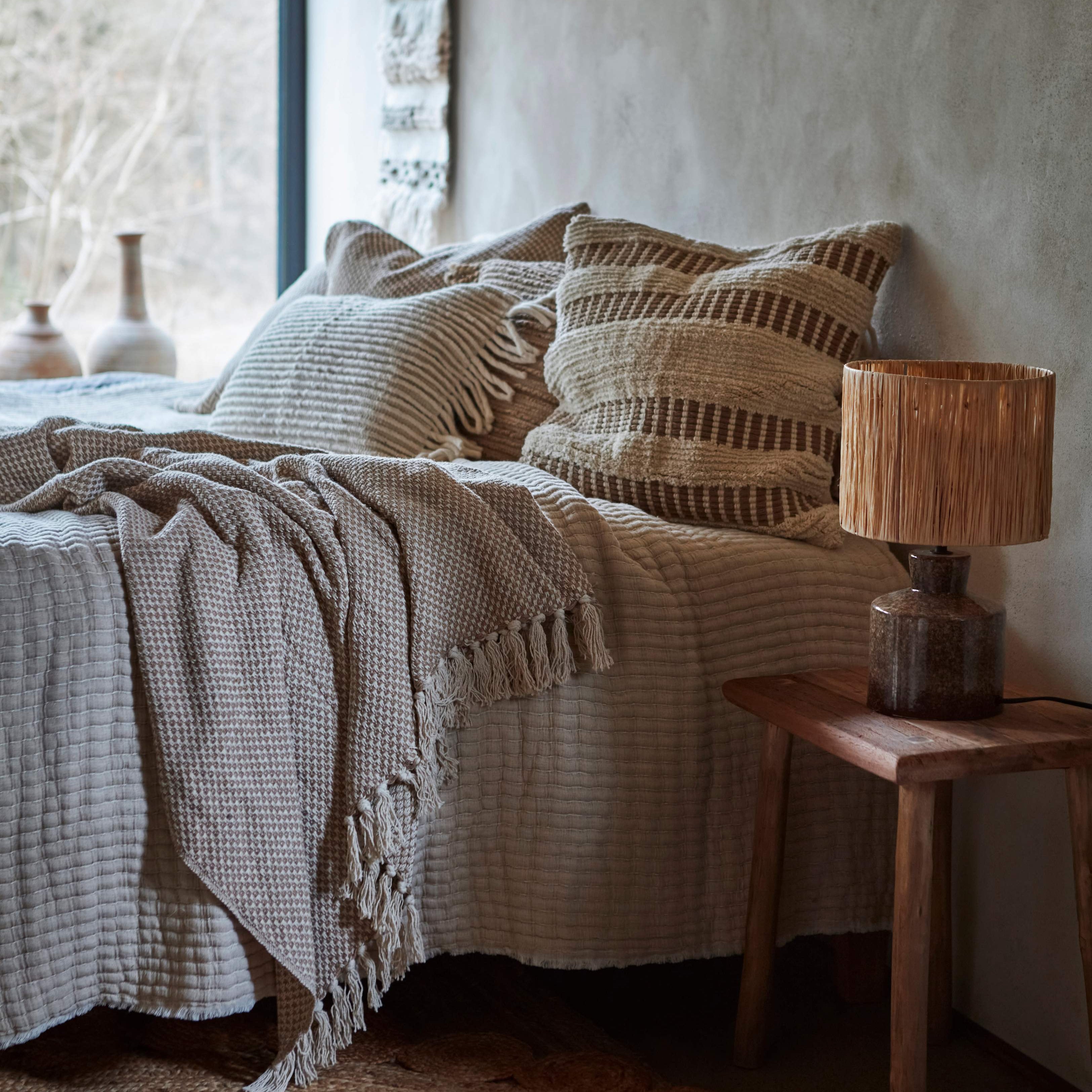 Cozs bedroom with textured bedding and stripe 50cm cushions, wooden nightstand with lamp 
