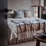 Cosy bedroom with a bed covered in a blanket and pillows, a side table with candles, and decor items.