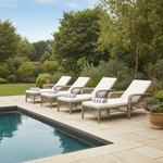 Four wicker lounge chairs with white cushions by a pool in a garden setting.