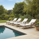 Four wicker lounge chairs with white cushions by a pool in a garden setting.