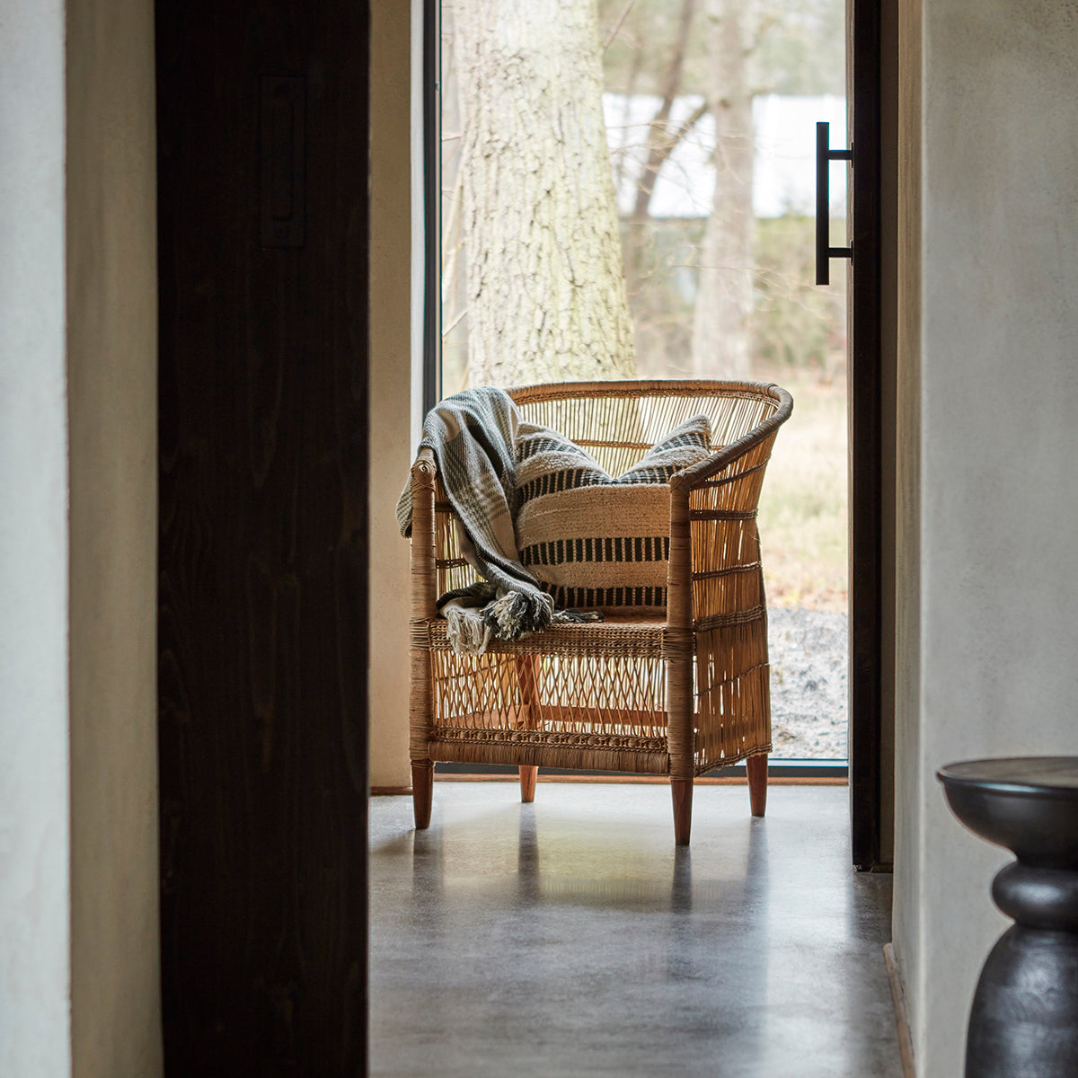 Wicker chair with a blanket and 50cm cushion n a room with a large window.