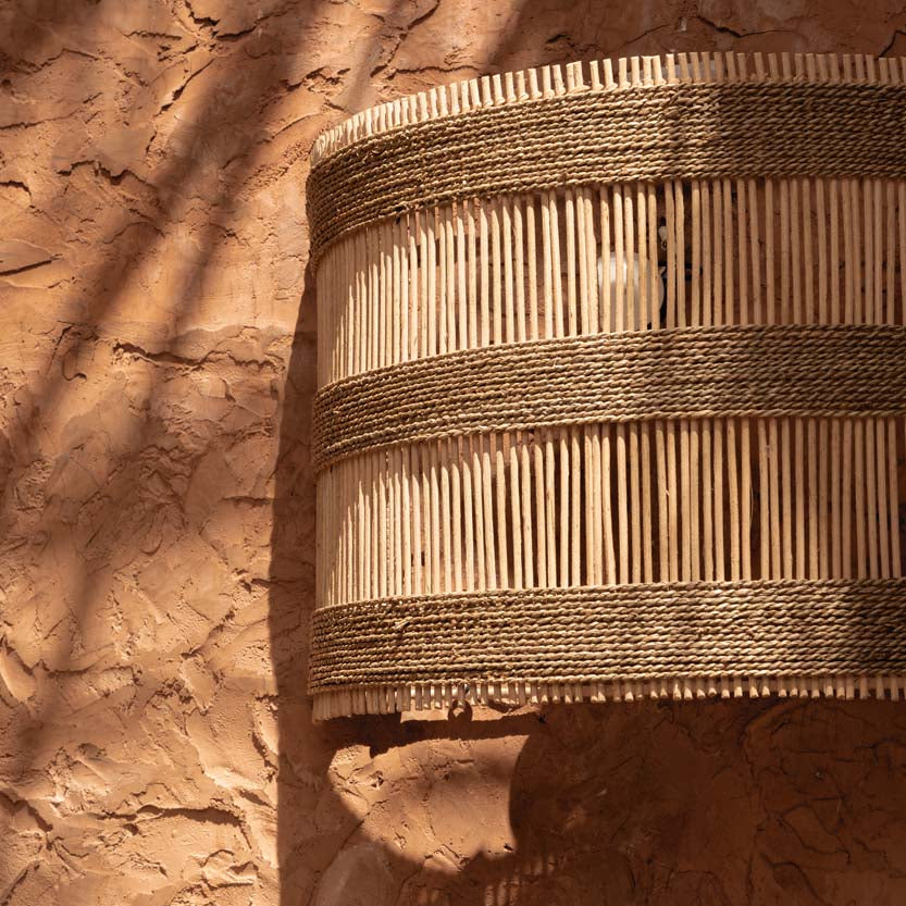 Woven rattan basket wall light shade outdoors against a textured brown wall