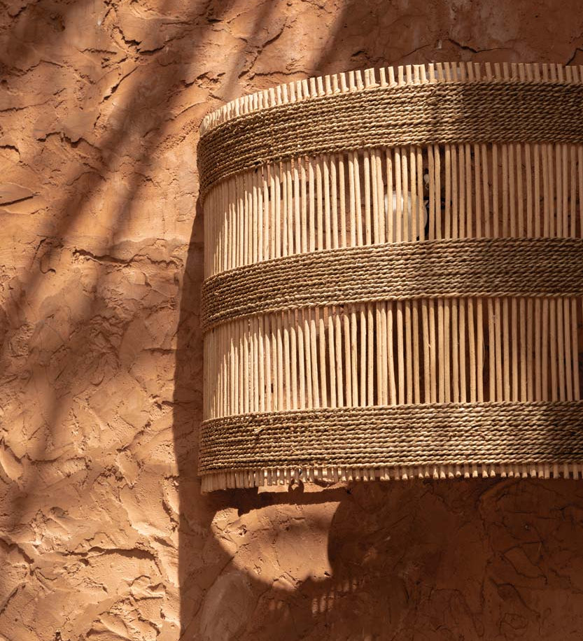 Woven rattan basket wall light shade outdoors against a textured brown wall