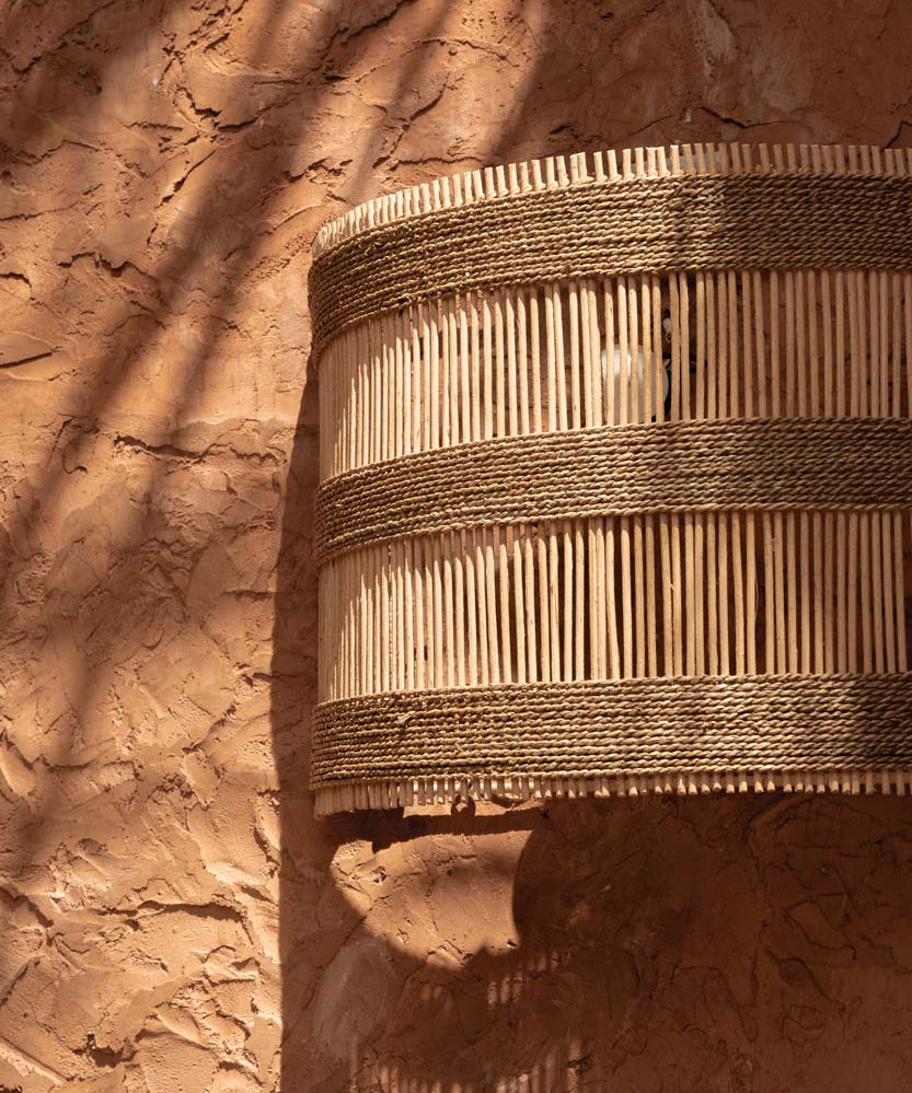 Woven rattan basket wall light shade outdoors against a textured brown wall