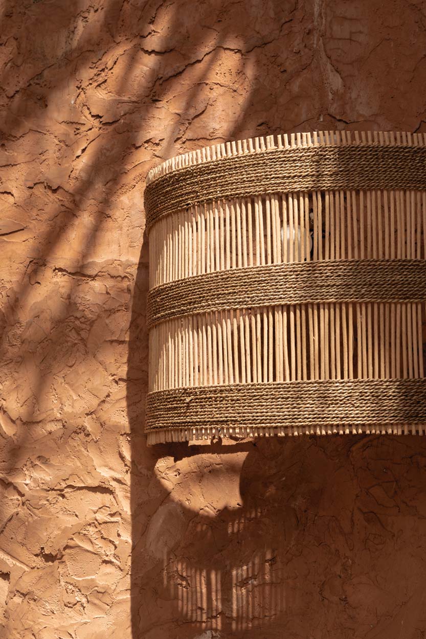Woven rattan basket wall light shade outdoors against a textured brown wall